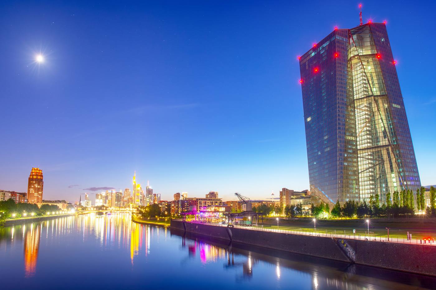 The European Central Bank tower in Frankfurt at night, with the moon and the skyline in the background