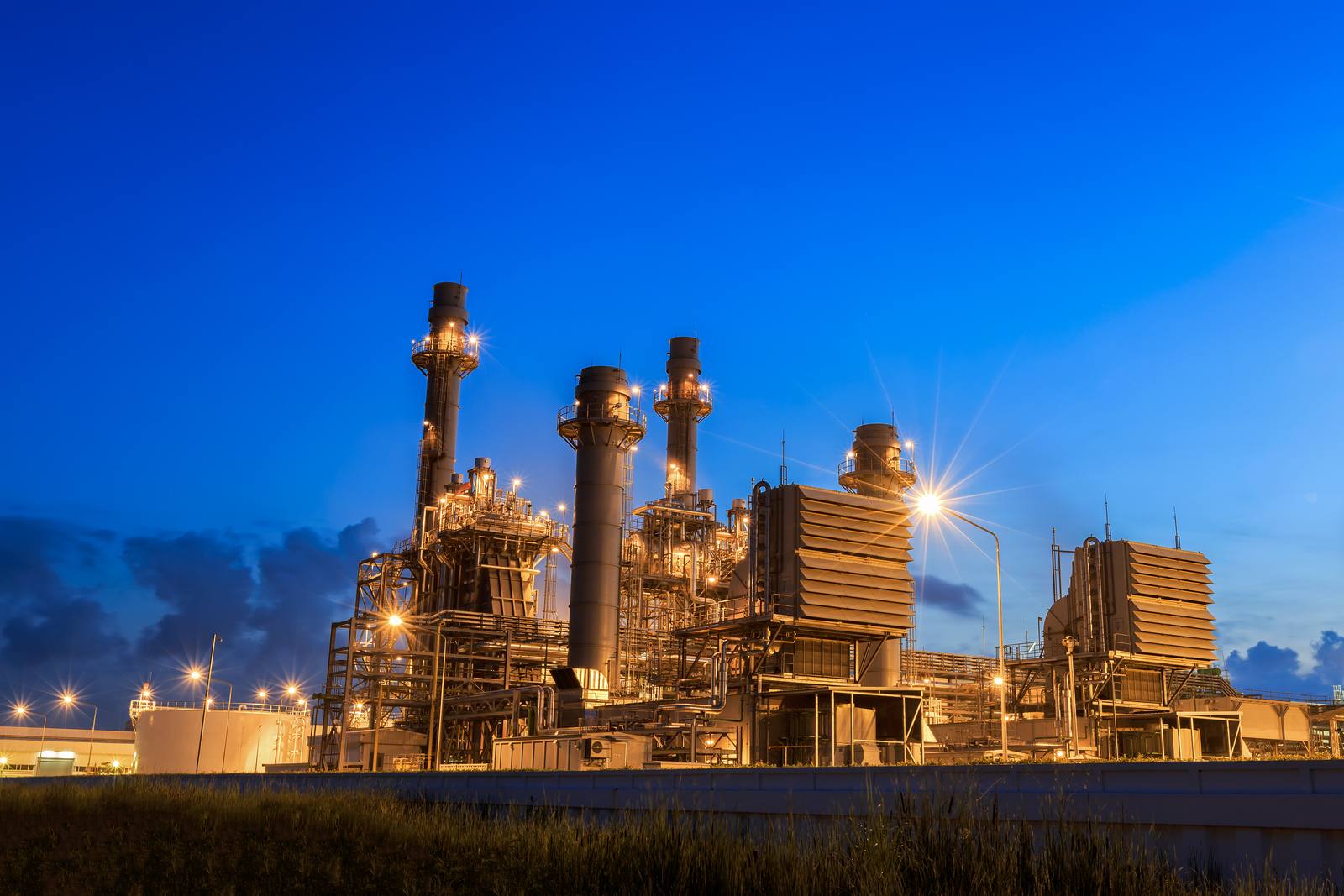 Verlichte gascentrale met schoorstenen tegen een donkerblauwe avondlucht