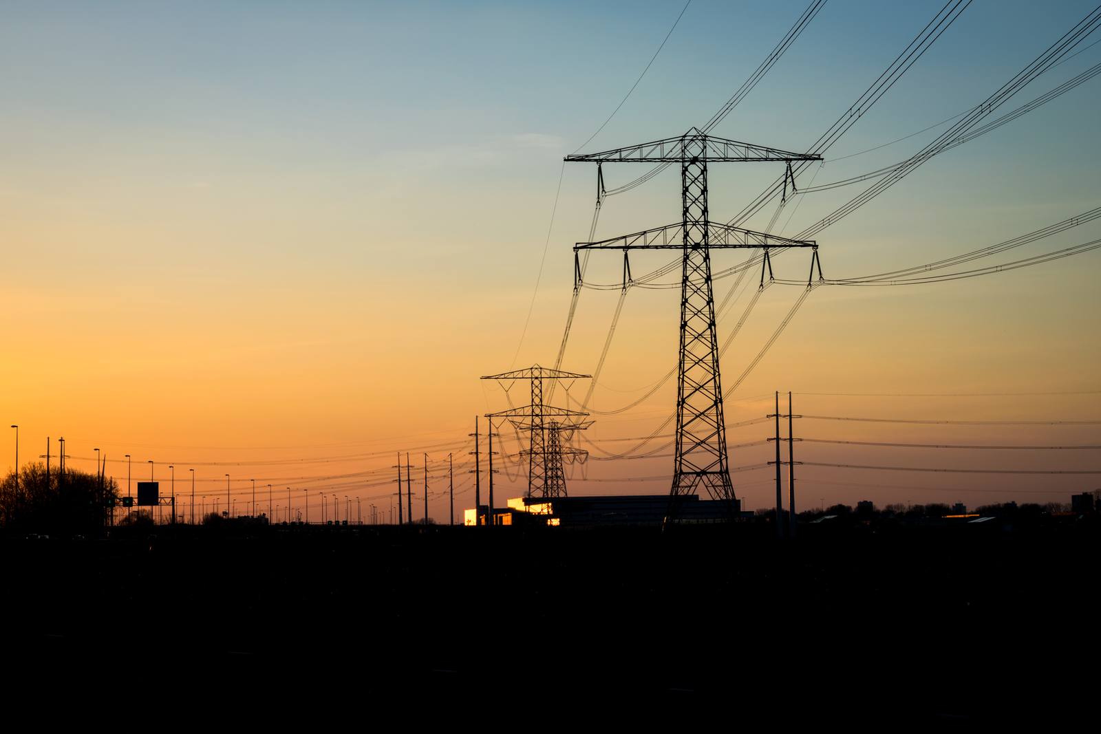 High-voltage pylons against an orange evening sky after sunset