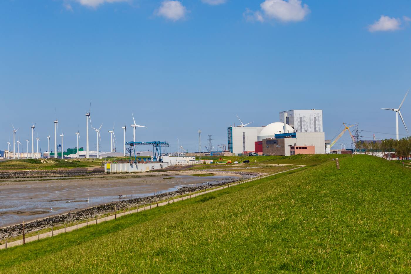 The nuclear power plant at Borssele behind a green dike, with wind turbines and a crane in the background