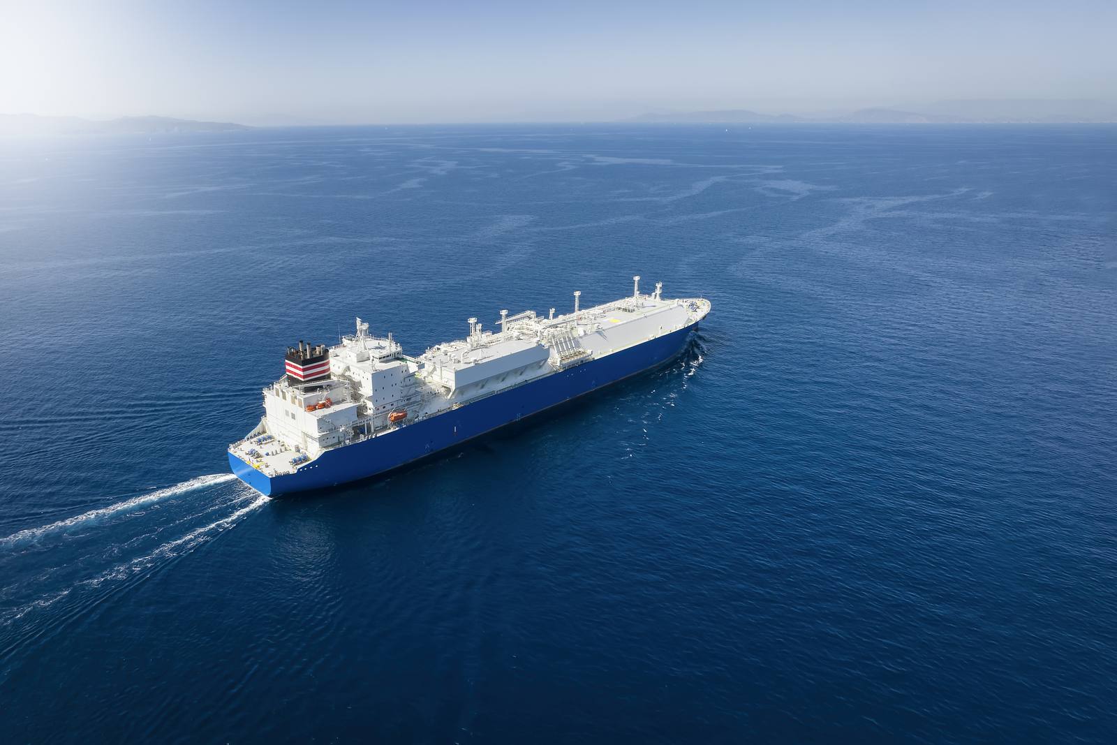 LNG tanker with white domed tank covers sailing across a deep blue sea, seen from above at an angle