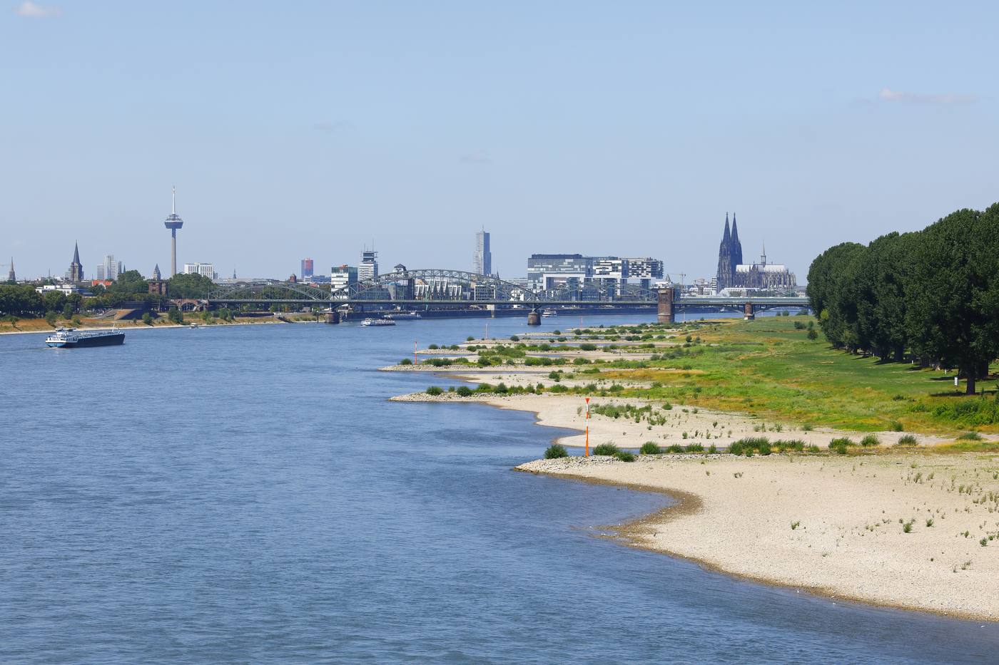 The Rhine at Cologne at low water with wide sandy banks, a cargo ship on the river and the cathedral in the background