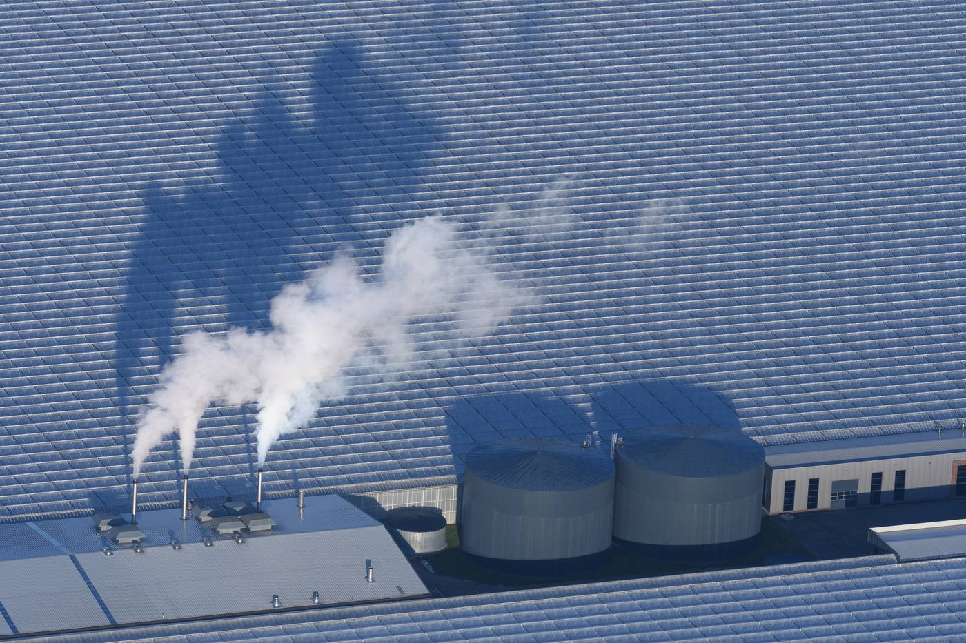 Luchtfoto van een glastuinbouwbedrijf met dampende schoorstenen en twee warmtebuffers